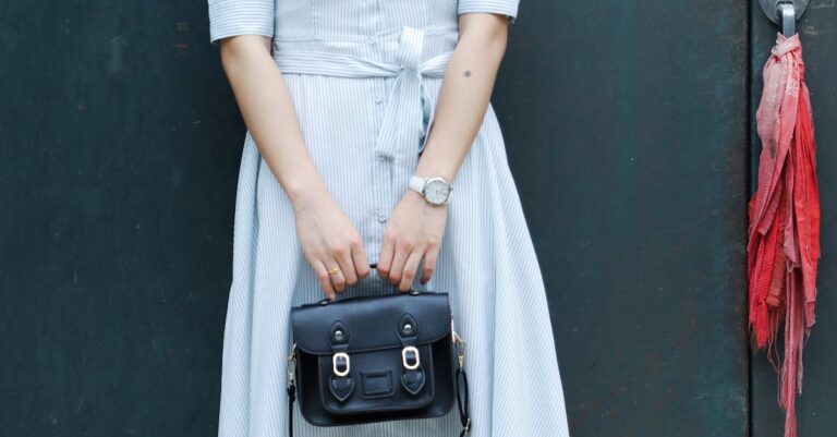 Mulher segurando uma bolsa preta, usando um vestido listrado.