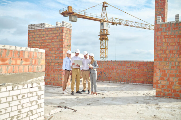 Por Que Alugar Equipamentos para Construção Sai Mais Barato Grupo de profissionais em um canteiro de obras, observando planta