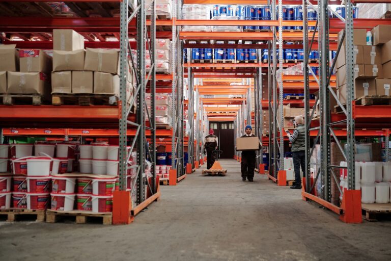 Trabalhadores circulam entre prateleiras altas cheias de caixas e produtos em um centro de distribuição de e-commerce